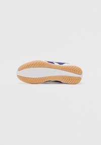 Suela de zapato con construcción de goma, predominantemente naranja y con un dibujo en el patrón de la superficie. Media suela blanca con ligera curvatura para soporte del arco.