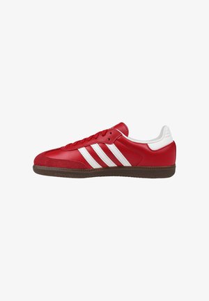 Sneaker rossa a profilo basso con strisce bianche, suola marrone, chiusura con lacci e colletto imbottito bianco sul tallone.