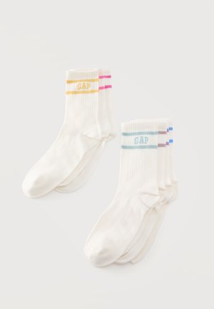 Deux paires de chaussettes blanches montantes avec des logos GAP et des rayures pastel, disposées sur un fond clair.