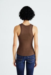 Bruine geribbelde tanktop met een aansluitend ontwerp, dikke schouderbanden en een gebogen zoom, gecombineerd met donkerblauwe jeans met achterzakken.