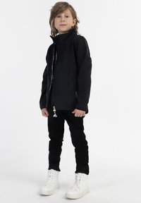Svart zip-up jacka med hög krage och kontrasterande inredning, tillsammans med svarta byxor och vita högre sneakers.