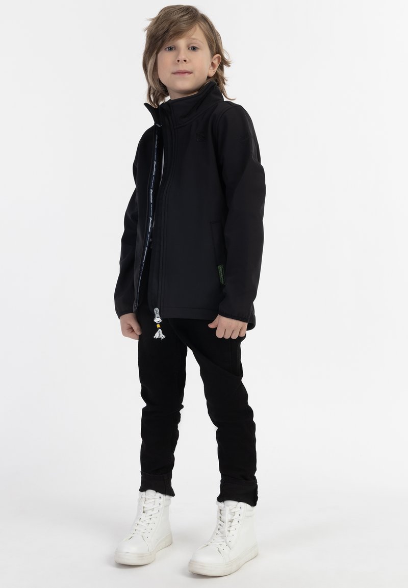 Svart zip-up jacka med hög krage och kontrasterande inredning, tillsammans med svarta byxor och vita högre sneakers.