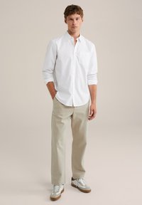 Witte overhemd met knopen en een zak, gecombineerd met beige relaxte broek en grijs-witte sneakers met bruine accenten. Eenvoudig ontwerp en materialen.