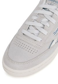 Sneaker in suede grigio chiaro con lacci bianchi, punta perforata e suola in gomma testurizzata. Presenta logo e accenti blu sul lato.