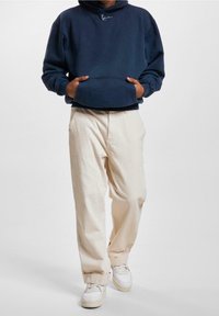 Námorně modrá mikina s kapucí a přední kapsou, spárovaná s krémovými volnými kalhotami a bílými teniskami.