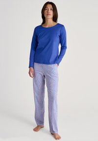Blauwe lange mouwen top gecombineerd met roze en blauwe verticaal gestreepte pyjamabroek. Glad materiaal, ontspannen pasvorm en zijzakken op de broek.