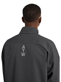 Man met kort krullend haar die een donker jasje draagt met verticale "ATW" letters op de bovenrug, weggekeken tegen een witte achtergrond.