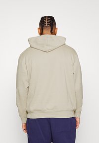 Felpa beige con cappuccio regolabile, realizzata in un tessuto morbido. Il design presenta una vestibilità comoda e polsini a coste.