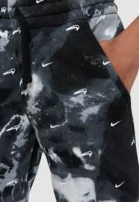 Svarta och grå sweatpants med ett molnmönster, prydda med små vita Nike-logotyper, elastisk midja och detaljer med sidofickor.