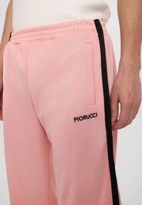 Ροζ φόρμες με ελαστική μέση, με μαύρη λωρίδα στο πλάι και το λογότυπο "Fiorucci" σε μαύρο χρώμα στο αριστερό μηρό. Λείο υλικό.