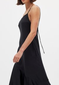 Mustat hihattomat mekot, joissa on tiukka vartalo ja laskostettu hame, sekä säädettävät soljet takana. Sujuva rakenne, minimalistinen muotoilu.