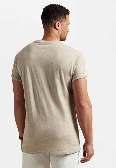 Bežs kokvilnas T-krekls ar uzrullētām piedurknēm, apaļu kakla izgriezumu un brīvu piegriezumu, ar gludu tekstūru un minimālām šuvju detaļām.