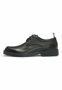 Scarpa in pelle nera con punta rotonda, design con lacci, suola in gomma nera testurizzata e stile minimalista. Presenta dettagli di cucitura.