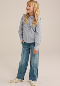 Prugasta srajca s nabranim dizajnom, kombinirana z širokimi jeans hlačami in belimi supergami z bež detajli.