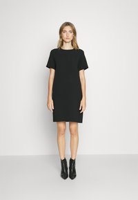 Black short-sleeve dress with a relaxed fit, featuring a round neckline and smooth fabric. Worn with black ankle boots.