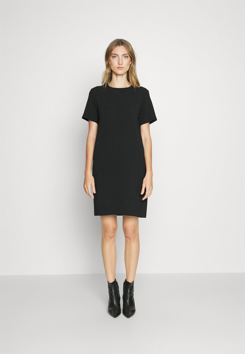 Black short-sleeve dress with a relaxed fit, featuring a round neckline and smooth fabric. Worn with black ankle boots.