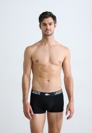 Boxers pour hommes noirs avec une large ceinture élastique arborant le logo "LACOSTE" et l'emblème du crocodile. Design lisse et ajusté.