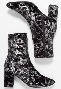 Bottines camouflage noires et argentées avec un tissu texturé, un bout pointu et un talon carré. Détail de fermeture éclair sur le côté.