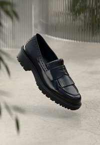 Navy siniset nahka loaferit frilla-tiedoilla, brogue-reikien kanssa ja paksu musta pohja. Sileä pinta kiiltävällä viimeistelyllä, minimalistinen muotoilu.