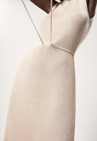 Robe en tricot côtelé de couleur beige doux, présentant une silhouette ajustée, des fines bretelles et une surface texturée avec une légère élasticité.