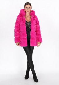 Faux fur coat in vibrant pink with hood, featuring a boxy design and plush texture. Worn over a black lace top and black leggings.
