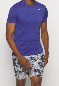 Lila kortärmad träningsskjorta med en strukturerad yta. Matchad med grå simshorts med ett svart abstrakt mönster och korallaccent.