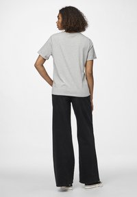 Grå t-skjorte med korte ermer, kombinert med brede svarte bukser og svarte joggesko. Stoffet ser mykt ut, med en avslappet passform.