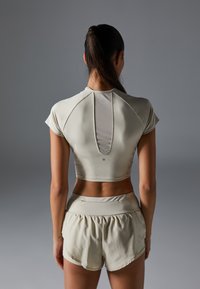 Light beige athletic set featuring a cropped top with a back cutout, short sleeves, and loose-fitting shorts with an elastic waistband.