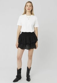 T-shirt blanc à manches courtes associé à une jupe noire en dentelle à volants et des bottines noires, avec une ceinture texturée et un design en couches.