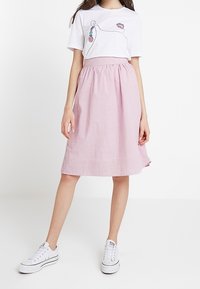 T-shirt blanc avec un dessin au trait et des pelotes de laine colorées, associé à une jupe rose rayée arrivant au genou et des baskets blanches.