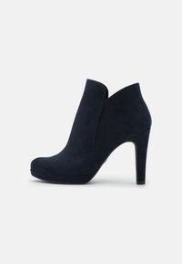 Botines de ante azul marino con una abertura acampanada, tacón alto de aguja y punta redondeada. Textura suave con un ligero brillo.