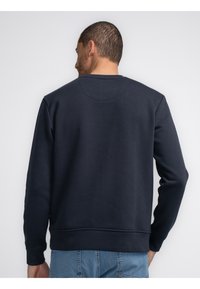 Marine sweater met een ronde hals, zachte textuur en geribde manchetten. Heeft een gladde achterkant en een ontspannen pasvorm.