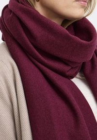 Bordový vlnený šál, hrubá a mäkká textúra, voľne omotaný okolo krku, v kombinácii so svetlom béžovým svetrom.