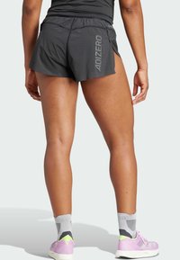 Melnas sporta šortus ar elpojošu tekstūru, ar sānu šķelmi, elastīgu jostu un "ADIZERO" logo aizmugurē.