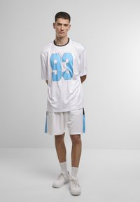 Maglia sportiva bianca con il numero blu "93" e accenti neri, abbinata a pantaloncini bianchi coordinati. Presenta maniche corte e una vestibilità comoda.