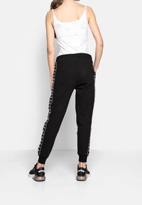 Zwarte joggers met een taps toelopende pasvorm, elastische tailleband en zijstrepen met een wit grafisch patroon. Gecombineerd met zwarte schoenen.