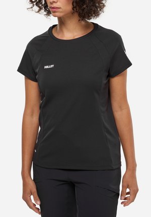 Femme portant un haut de sport noir à manches courtes avec le logo "MILLET" sur la poitrine, assorti à un pantalon noir, sur un fond uni.