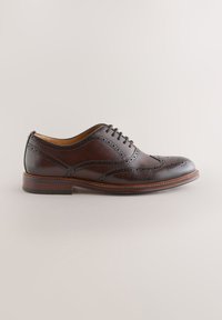 Dunkelbrauner Leder-Brogue-Schuh mit Flügelkappen-Perforationen und geschlossener Schnürung auf neutralem Hintergrund.