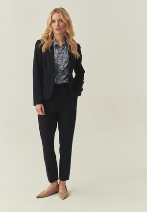 Marineblauw colbert en broek gecombineerd met een blauw bloemenblouse. Beige slingback schoenen met een puntige neus. Soepele stof en een getailleerde pasvorm.