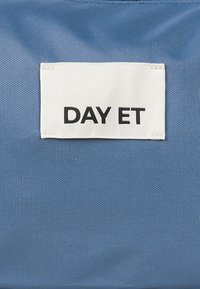 Blå stof med et hvidt mærke, hvor der står "DAY ET" trykt med fed sort tekst. Materialet ser glat ud med en subtil tekstur.