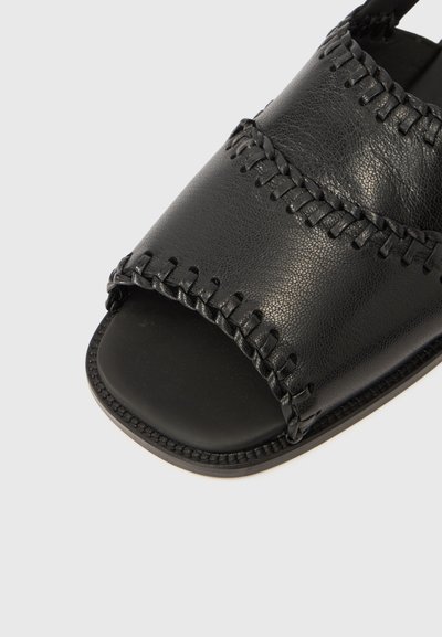 Μαύρο δερμάτινο σανδάλι με ανοιχτό δάχτυλο, με πλεκτή ραφή στο πάνω μέρος και λείο, επίπεδο πέλμα. Υφή στο υλικό.
