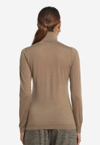 Brauner, taillierter Rollkragenpullover aus einem weichen, leichten Material. Lange Ärmel, ribbeliger Kragen und Bündchen. Kombiniert mit gemusterten Hosen.