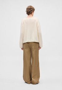 Kremowy sweter z dzianiny z opuszczanymi ramionami, w połączeniu z szerokimi beżowymi spodniami z tylnymi kieszeniami i gładką fakturą.