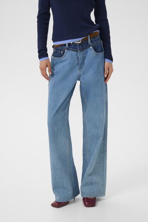Jeans in denim blu chiaro a gamba larga con una finitura sbiadita, dotati di cinque tasche e una cintura marrone, abbinati a un maglione in navy a coste.