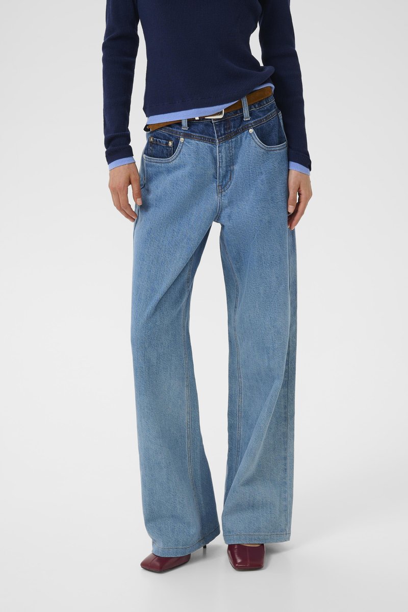 Light blue wide-leg denim jeans with a faded finish, featuring five pockets and a brown belt, paired with a navy ribbed sweater.