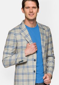 Beżowa marynarka w kratę z niebieskimi liniami, z klapami w kształcie notcha, dwoma guzikami i teksturowanym materiałem, noszona na niebieskiej koszulce.