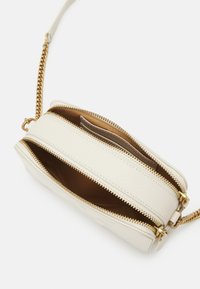 White leather crossbody bag with gold hardware, featuring two zippered compartments and a chain strap. Interior has brown lining.