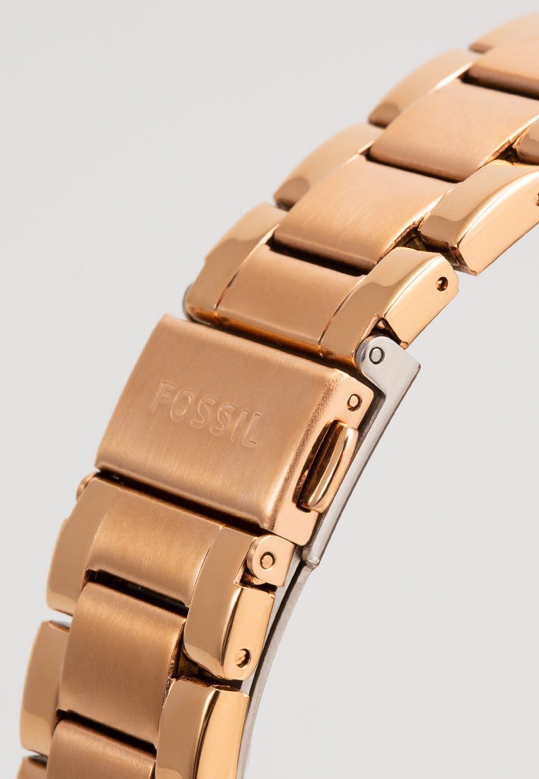 Roze gouden metalen horlogeband met gepolijste schakels, voorzien van een sluiting met gegraveerd "FOSSIL." Glad oppervlak met een slank ontwerp.