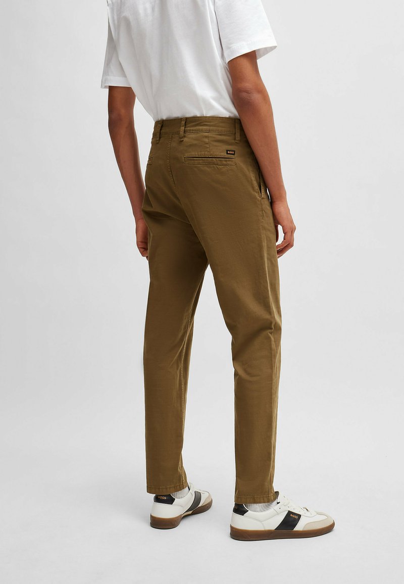 Pantalons kaki à coupe droite, avec un détail de poche arrière, assortis à des baskets blanches avec des accents noirs. T-shirt blanc uni au-dessus.