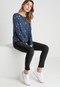 Maglietta a maniche lunghe blu navy con motivo floreale, abbinata a jeans skinny neri e scarpe da ginnastica bianche. Design semplice e texture morbida.